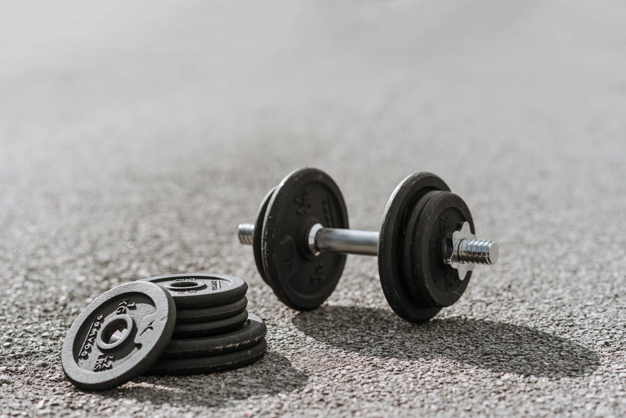 A black dumbbell and weights on an asphalt pavement, perfect for outdoor fitness themes.